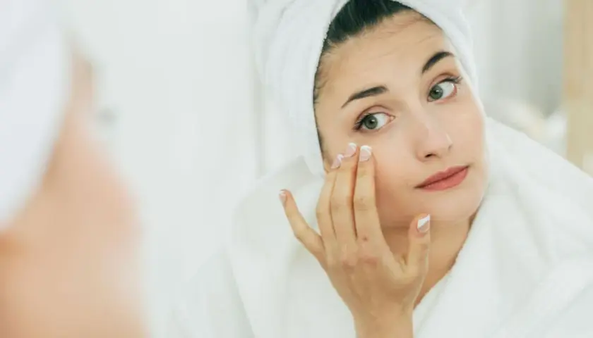 Mujer con toalla en la cabeza aplicándose crema, buscando productos que significan no comedogénico para cuidar su piel.