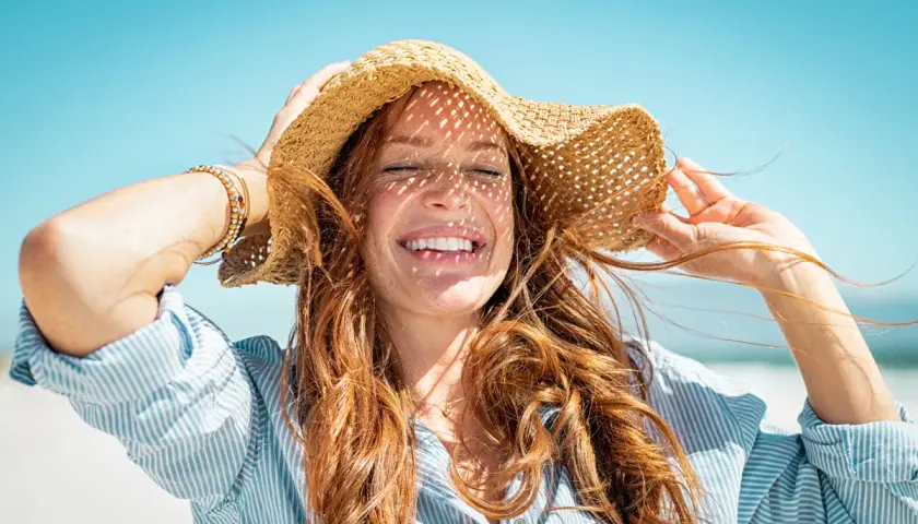 Mujer sonríe con sombrero de paja, aprendiendo como cuidar el pelo en verano.
