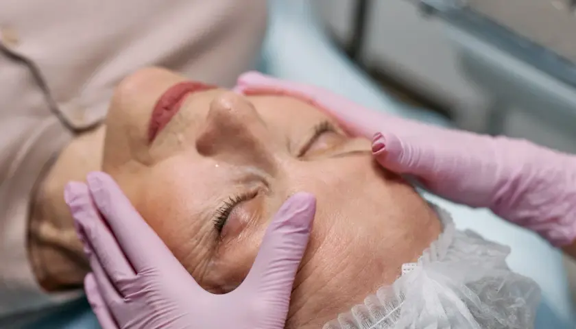 Manos enguantadas realizan tratamiento de radiofrecuencia en la cara de una mujer, buscando rejuvenecer su piel.