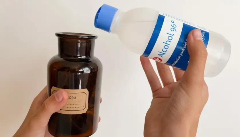 Manos vierten alcohol de romero en un frasco de vidrio ámbar. El alcohol de romero sirve para desinfectar y aliviar dolores.