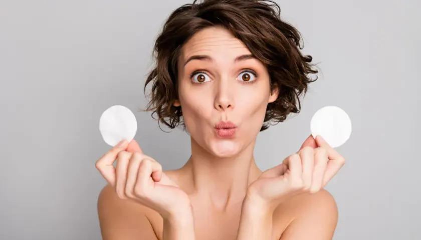 Mujer sorprendida con discos de algodón, mostrando para que sirve el agua micelar para una limpieza facial suave y efectiva.