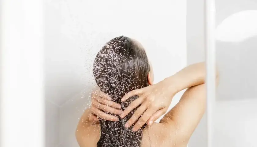 Persona disfrutando de un refrescante lavado de pelo bajo la ducha, con el agua cayendo sobre su cabello oscuro y las manos masajeando suavemente.