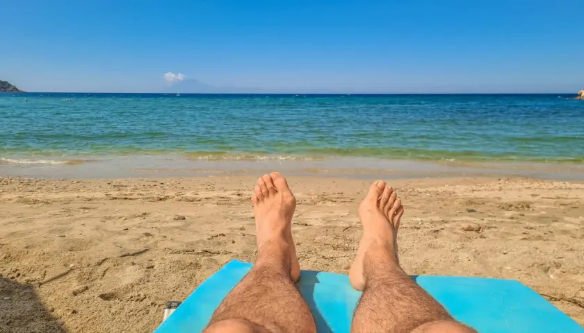Piernas bronceándose en la playa. El sol de las 7 de la tarde pone moreno mientras disfrutas del mar azul y la arena dorada.
