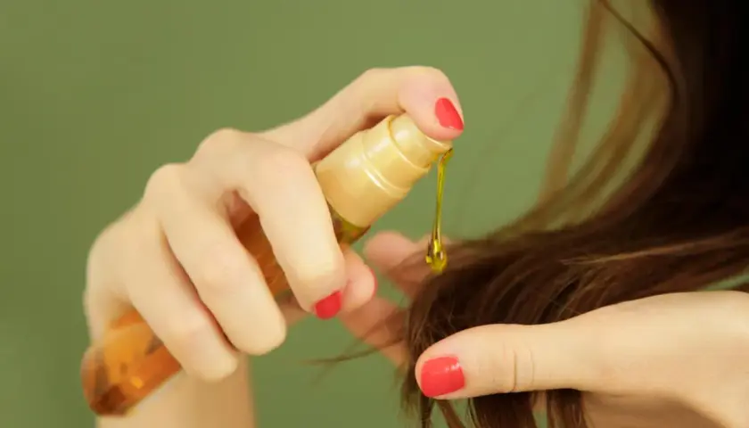 Manos aplicando aceite de ricino para el pelo, una gota dorada cae sobre las puntas.