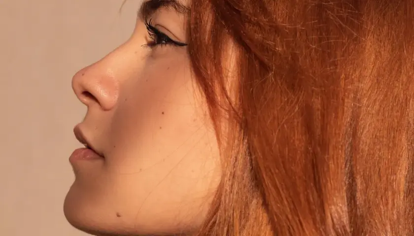 Perfil de mujer con cabello rubio cobrizo claro con mechas, delineado de ojos y pecas.