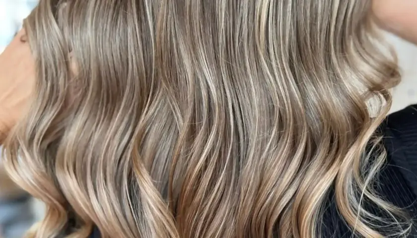 Cabello castaño con reflejos rubios sutiles, como baby lights, que le dan un toque natural y luminoso.