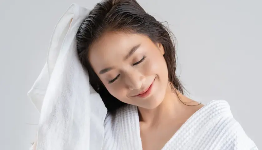 Mujer secándose el pelo con una toalla blanca. Recuerda, es malo dormir con el pelo mojado.