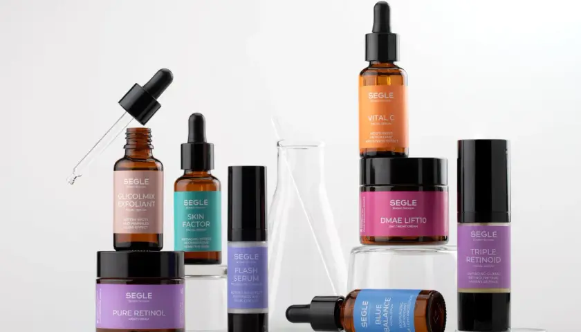Varias botellas y tarros de productos de cuidado de la piel Segle, incluyendo el serum cuando se aplica, sobre un fondo blanco.