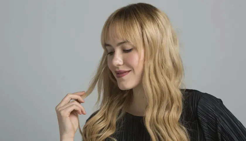 Mujer rubia con ondas, tocando su cabello. Aprende como matizar el pelo con tinte en casa para un look radiante.
