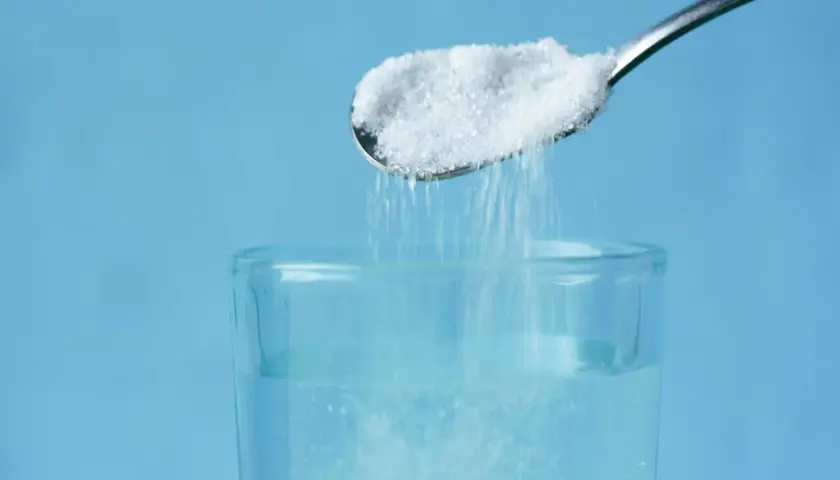 Cuchara con sal cayendo en un vaso de agua, un método para aclarar el pelo de forma natural.