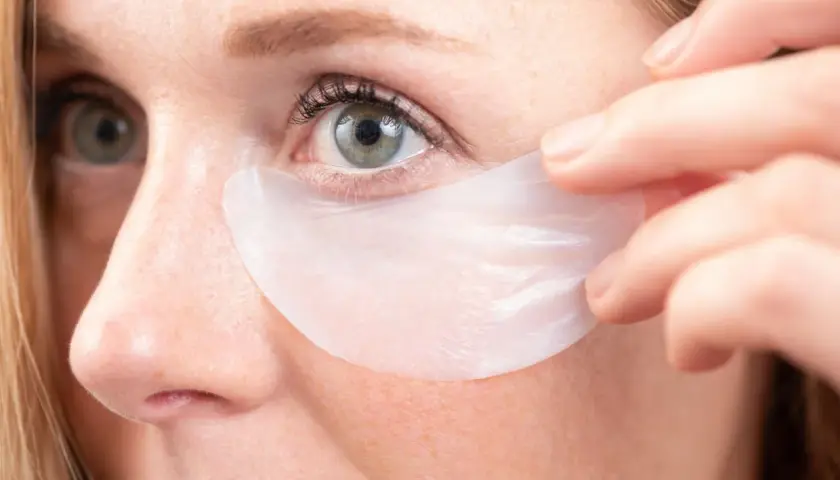 Aplicación de parches para el contorno de ojos. Una mujer se coloca un parche debajo del ojo para hidratar y revitalizar la piel.