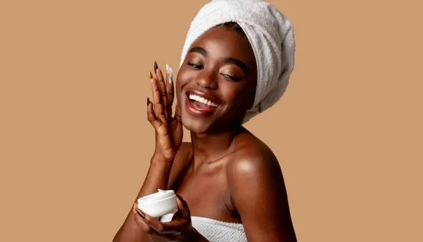 Mujer sonriente con toalla en la cabeza aplica crema con niacinamida y ácido salicílico.