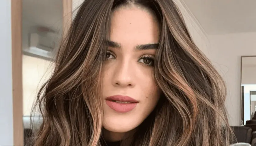 Mujer con cabello castaño oscuro y ondas suaves, resaltado por mechas shatush que aportan luz y dimensión.