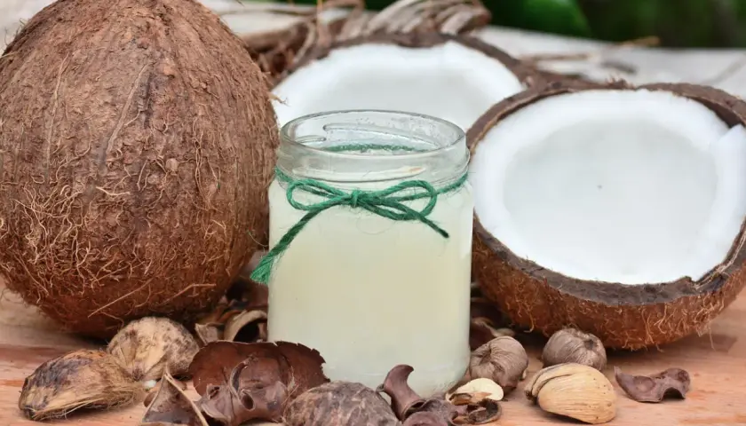 Aceite de coco para que sirve: un frasco de aceite de coco rodeado de cocos enteros y partidos, ideal para la piel y el cabello.