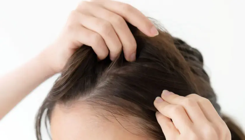 Manos revisando el cuero cabelludo, buscando remedios caseros para fortalecer el pelo fino y mejorar su volumen.
