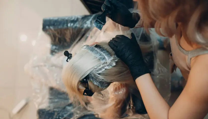 Manos enguantadas aplican tinte al cabello rubio. Es tiempo de tinte pelo para un cambio de look.