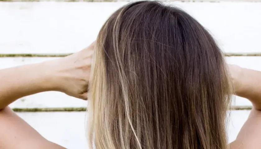 Cabello castaño con reflejos rubios, con las manos detrás de la cabeza.