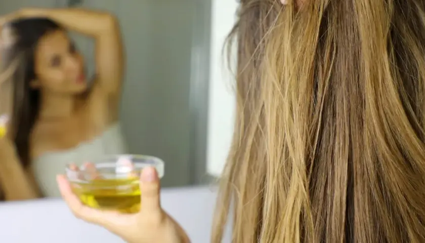Mujer se aplica aceite de oliva en el pelo, demostrando que el aceite de oliva es bueno para el pelo.