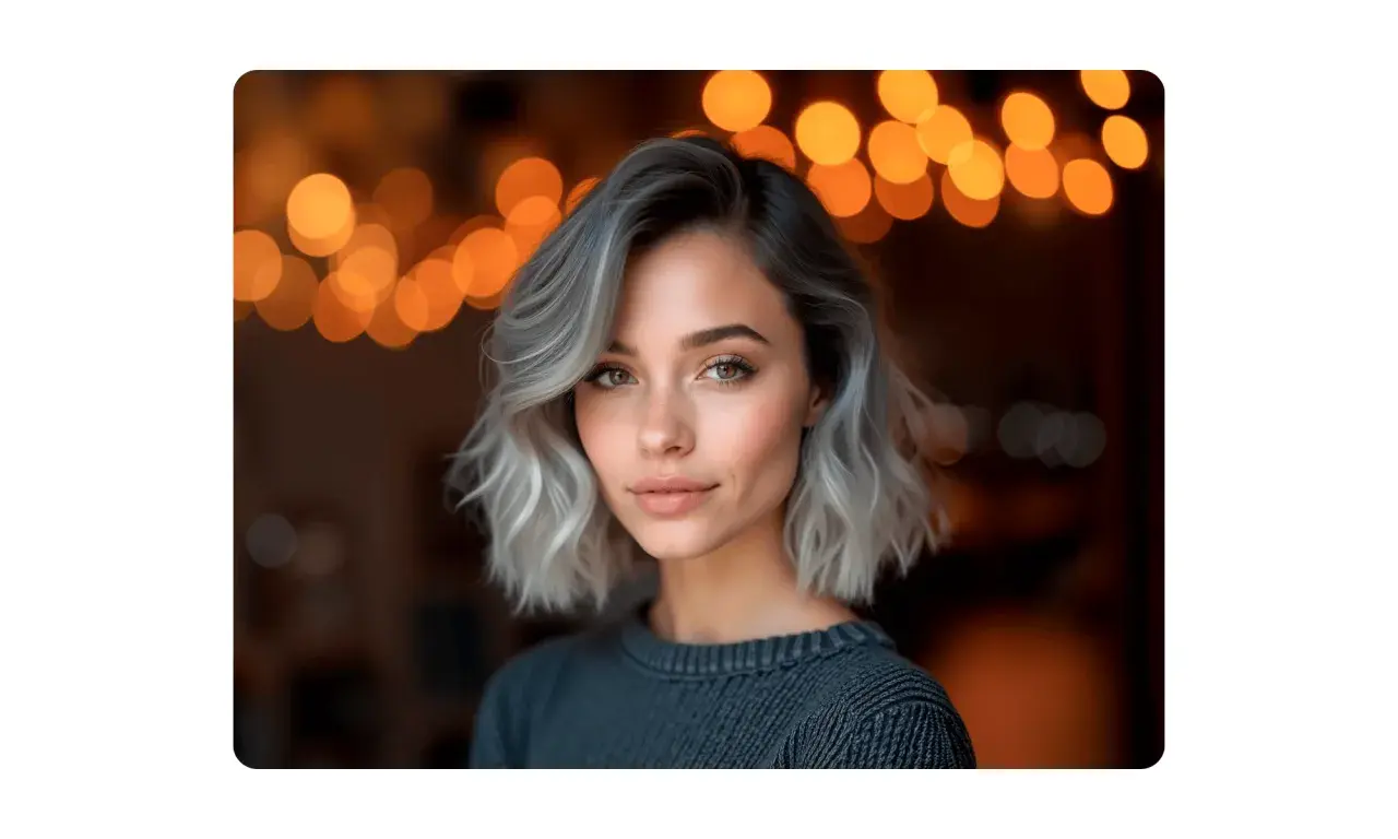 Mujer con pelo corto rubio platino ceniza, mirada cautivadora y luces cálidas de fondo.
