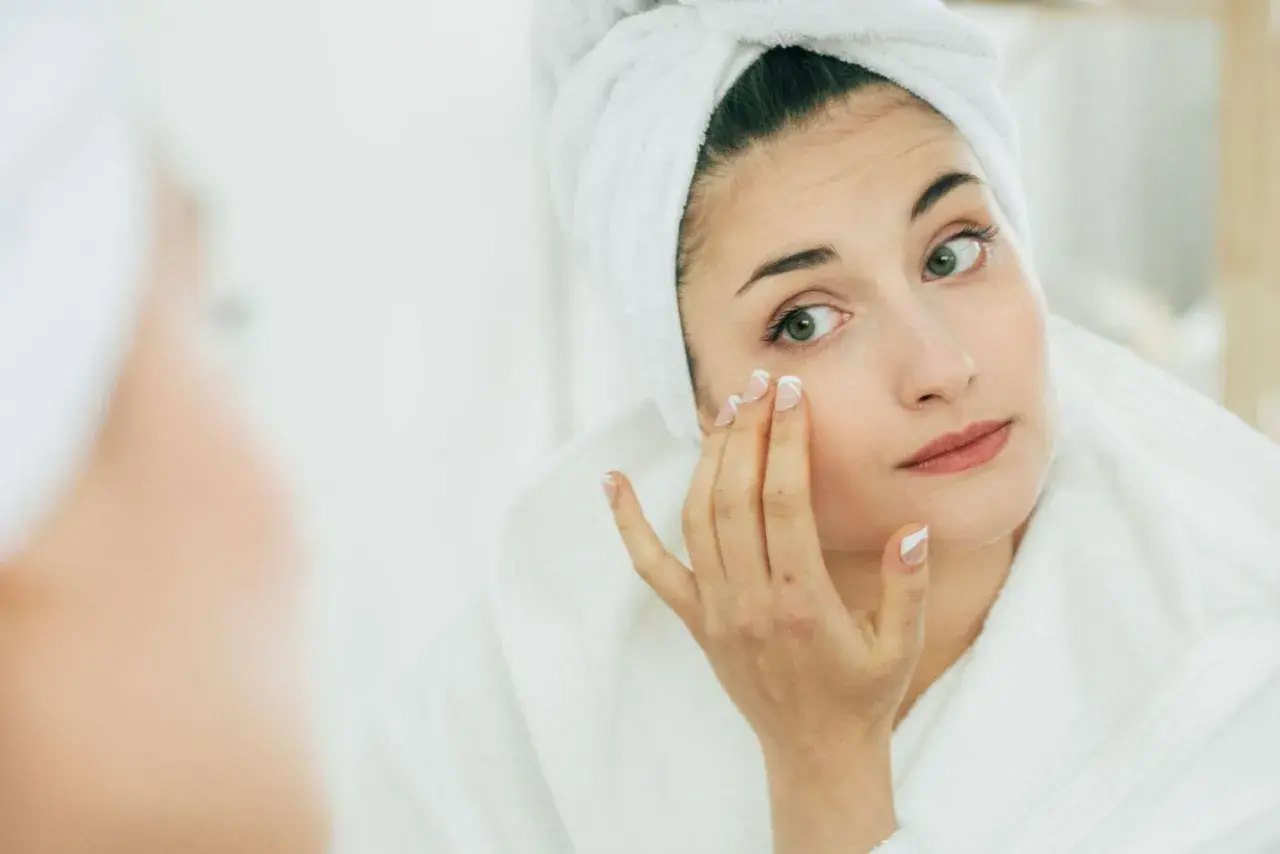 Mujer con toalla en la cabeza aplicándose crema, buscando productos que significan no comedogénico para cuidar su piel.