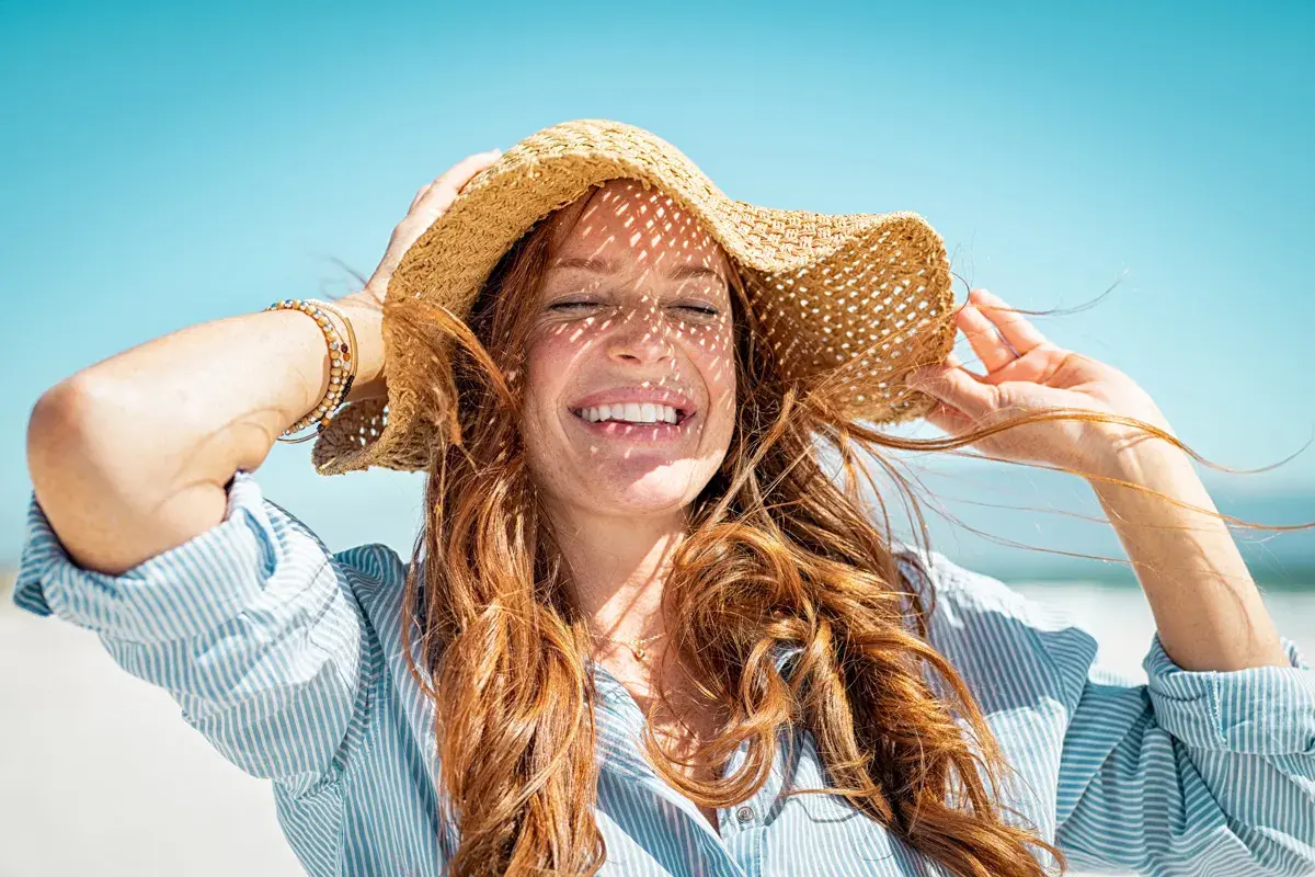 Mujer sonríe con sombrero de paja, aprendiendo como cuidar el pelo en verano.