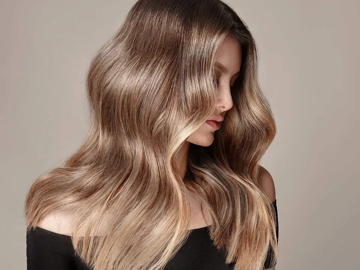 Mujer con cabello largo y ondulado, con un degradado de color que va de oscuro a rubio. Un ejemplo de cómo aclarar el pelo teñido para un look natural.