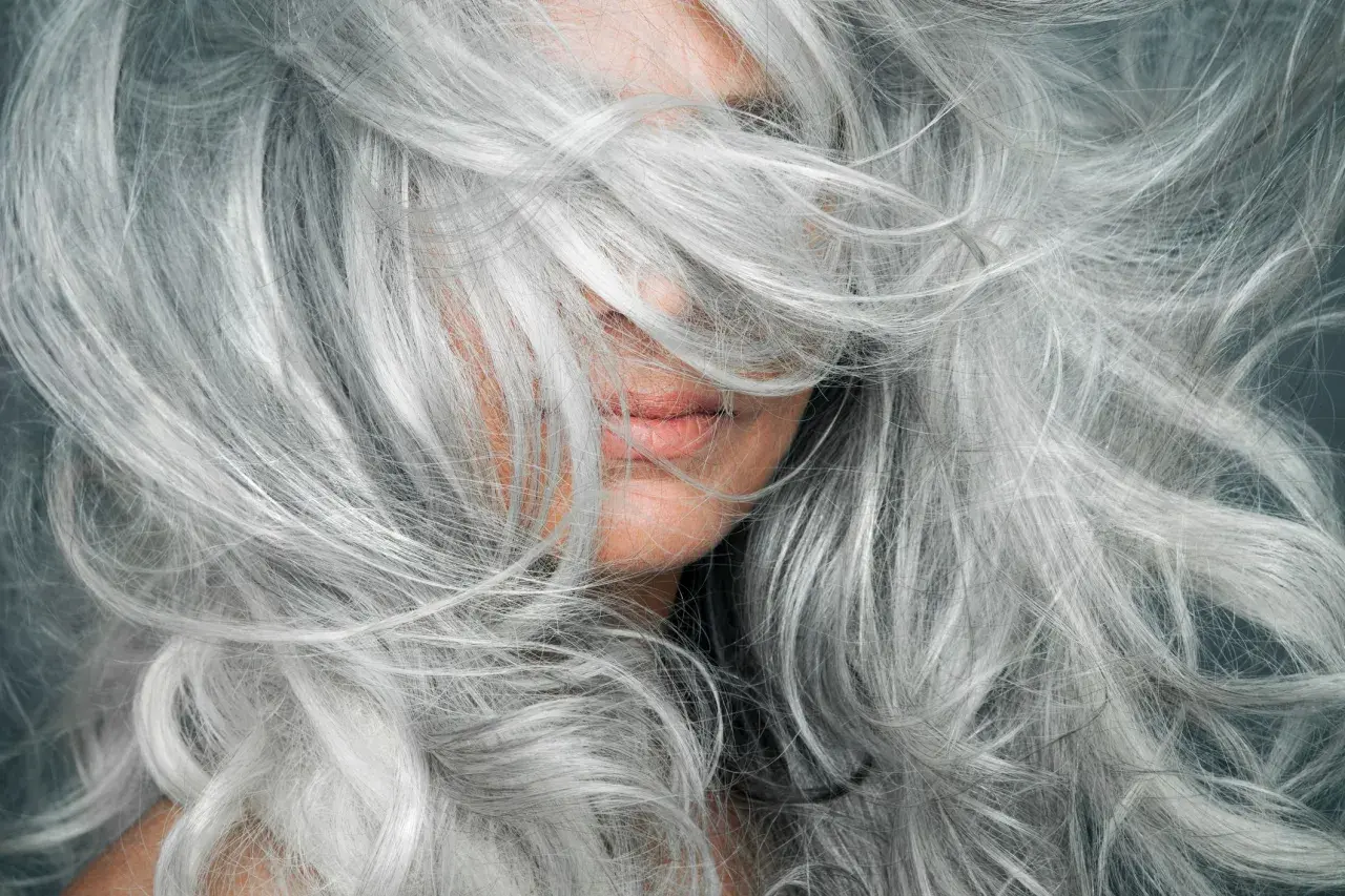 Una mujer con una cascada de cabello plateado, mostrando la belleza de la transición a canas.
