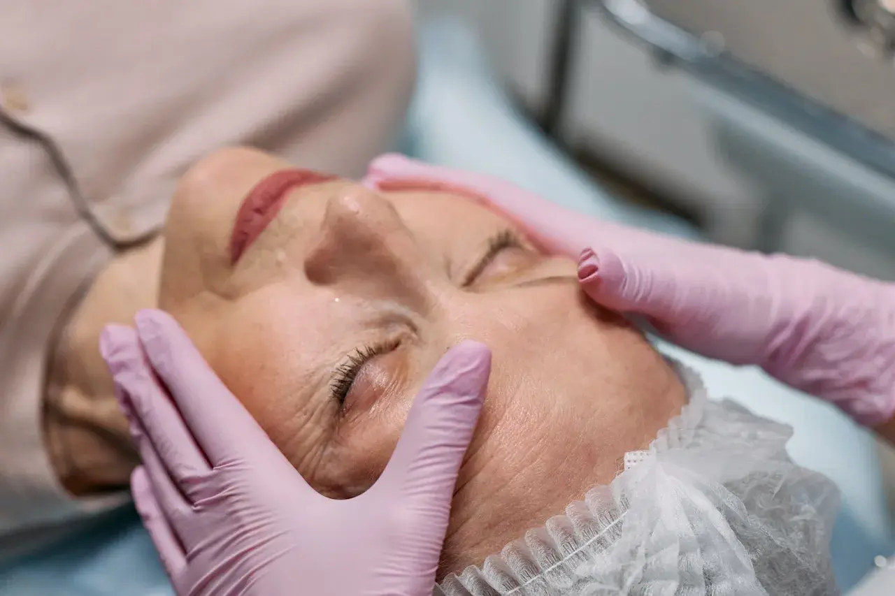 Manos enguantadas realizan tratamiento de radiofrecuencia en la cara de una mujer, buscando rejuvenecer su piel.
