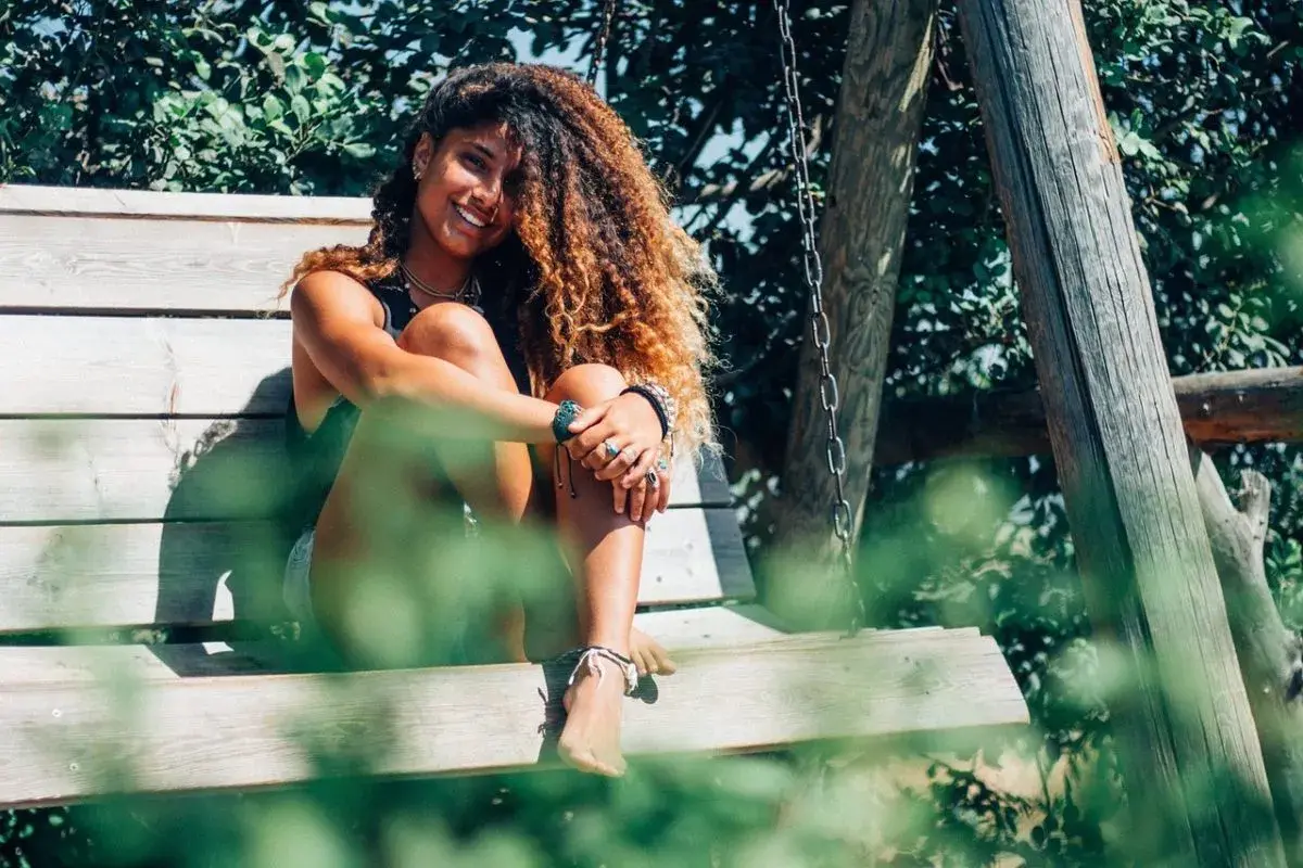 Chica con pelo rizado y voluminoso, sonriendo sentada en un columpio. ¡Así se consigue como rizar el pelo con espuma!