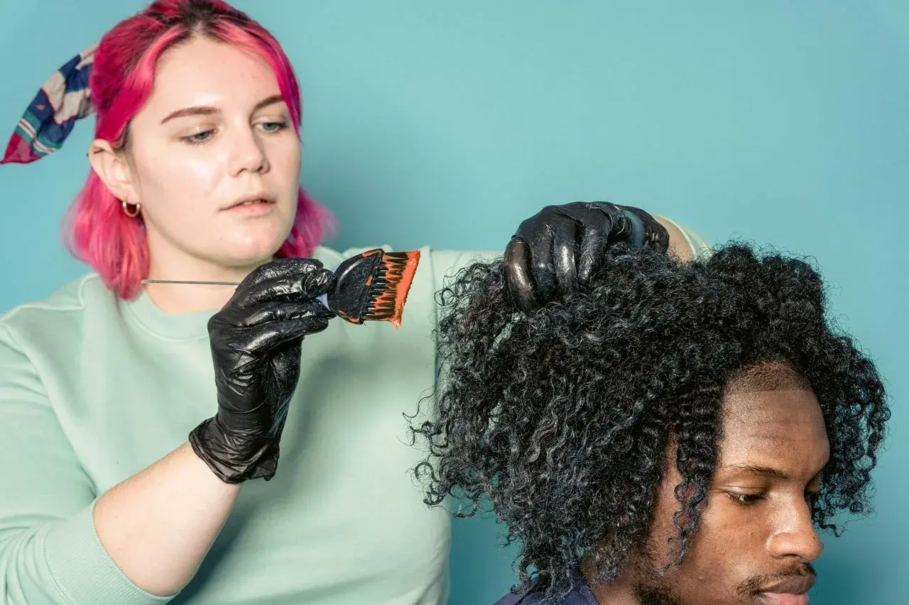 Mujer con pelo rosa aplica tinte a cabello rizado. ¿Cuánto dura un tinte de pelo? Depende del cuidado.
