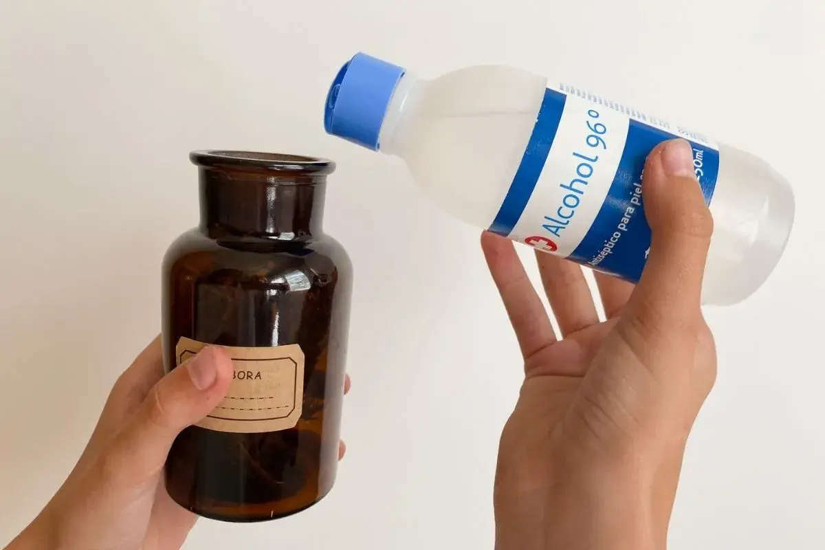 Manos vierten alcohol de romero en un frasco de vidrio ámbar. El alcohol de romero sirve para desinfectar y aliviar dolores.