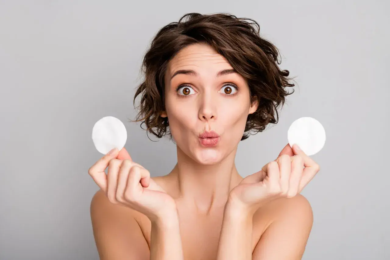 Mujer sorprendida con discos de algodón, mostrando para que sirve el agua micelar para una limpieza facial suave y efectiva.