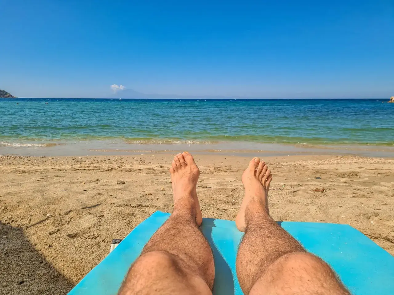 Piernas bronceándose en la playa. El sol de las 7 de la tarde pone moreno mientras disfrutas del mar azul y la arena dorada.