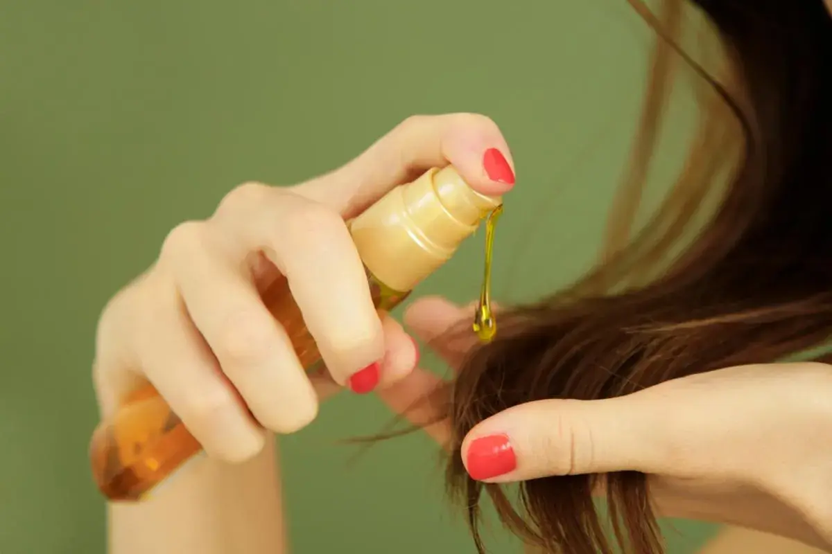 Manos aplicando aceite de ricino para el pelo, una gota dorada cae sobre las puntas.