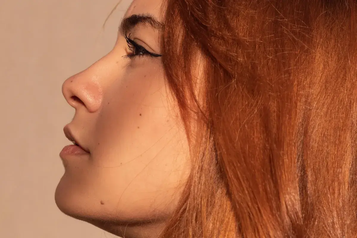 Perfil de mujer con cabello rubio cobrizo claro con mechas, delineado de ojos y pecas.