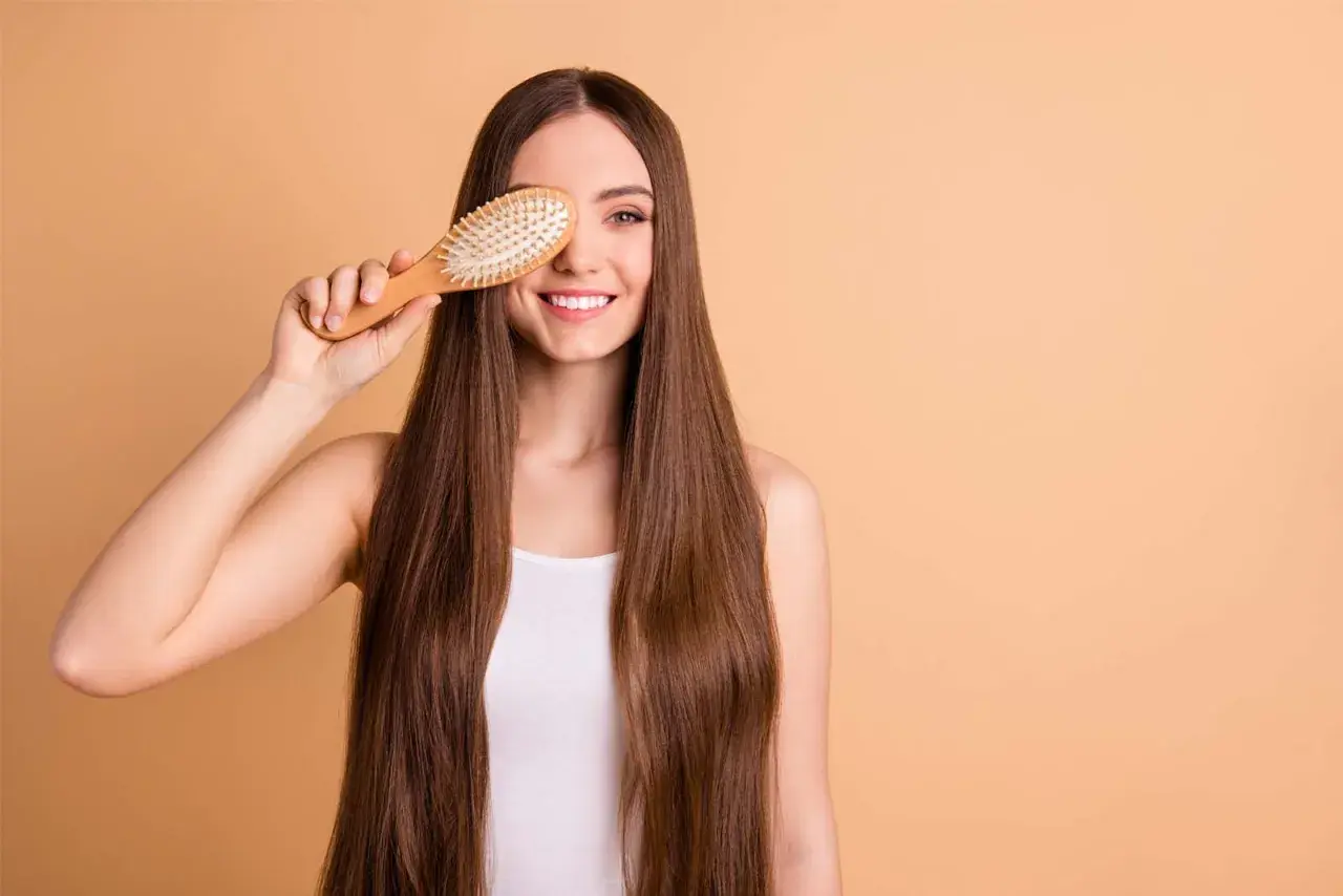 Mujer sonriente con pelo largo y liso, usando un cepillo de madera para mostrar cómo desenredar un pelo muy enredado.