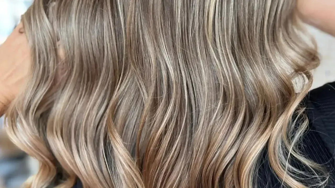 Cabello castaño con reflejos rubios sutiles, como baby lights, que le dan un toque natural y luminoso.