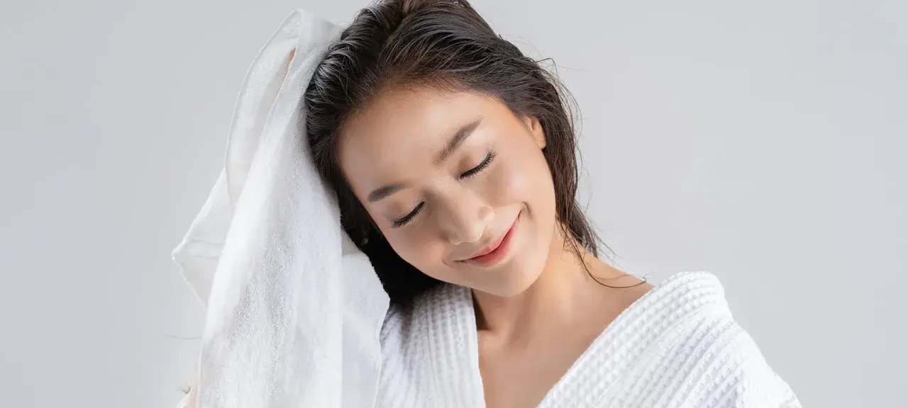 Mujer secándose el pelo con una toalla blanca. Recuerda, es malo dormir con el pelo mojado.