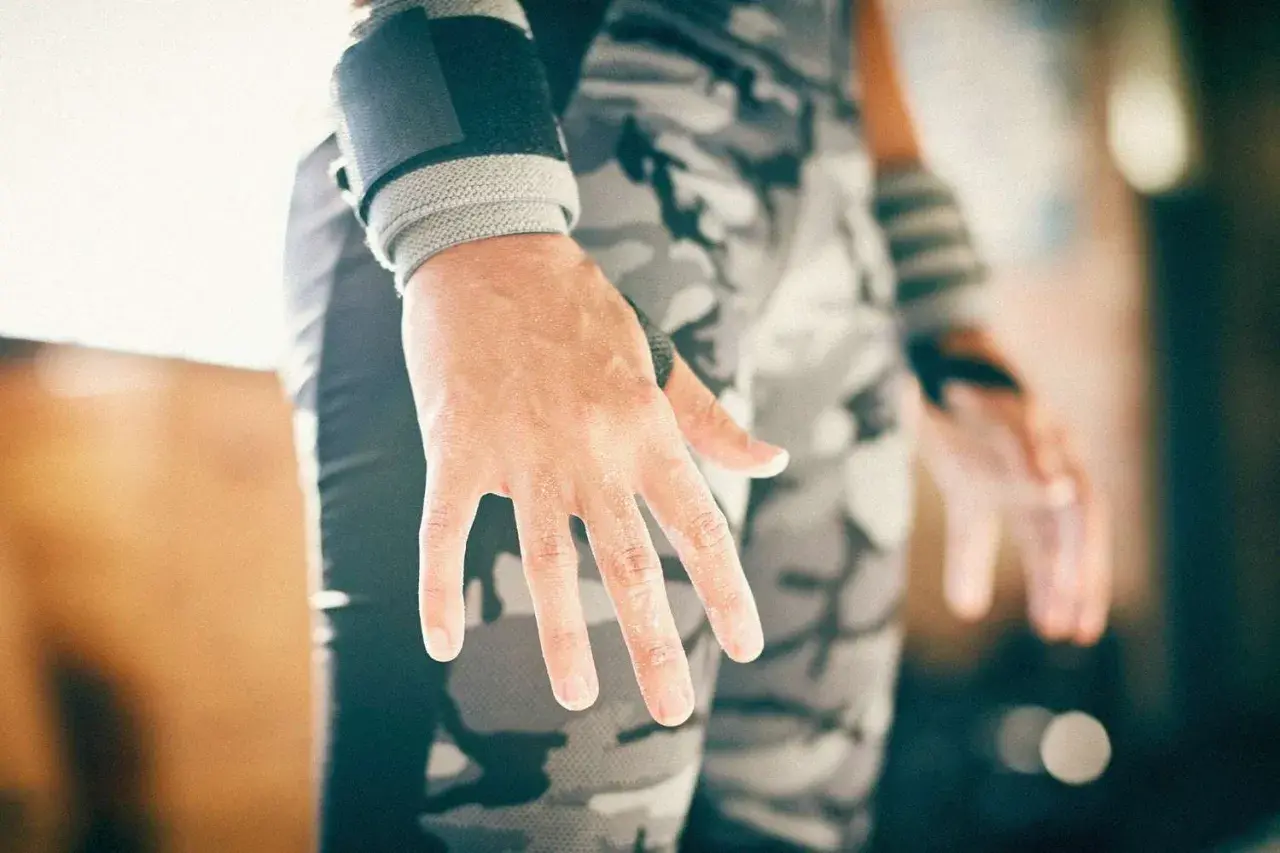 Manos con callos en los dedos, evidencia de entrenamiento duro. Muñequeras y pantalón de camuflaje completan la imagen.