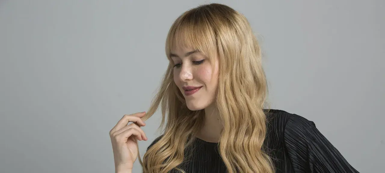 Mujer rubia con ondas, tocando su cabello. Aprende como matizar el pelo con tinte en casa para un look radiante.