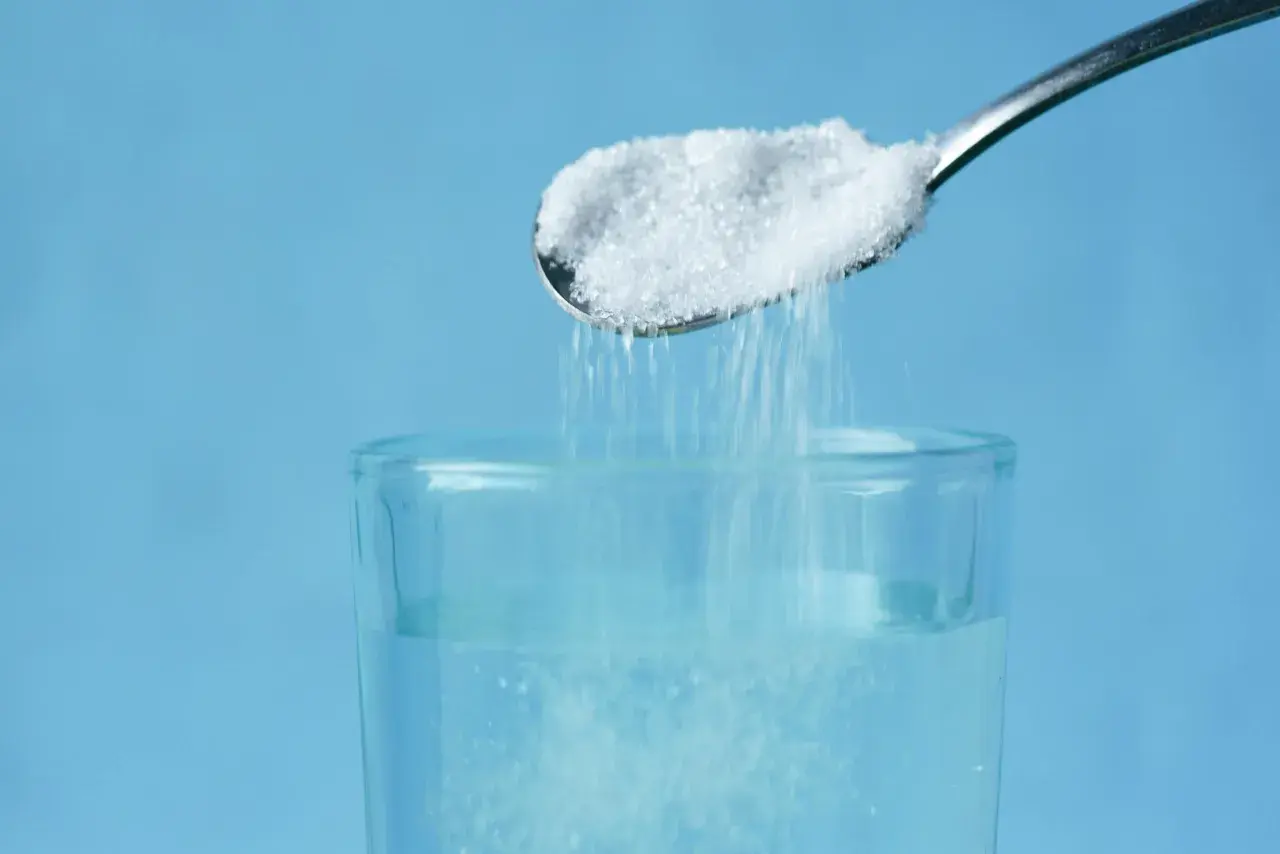 Cuchara con sal cayendo en un vaso de agua, un método para aclarar el pelo de forma natural.