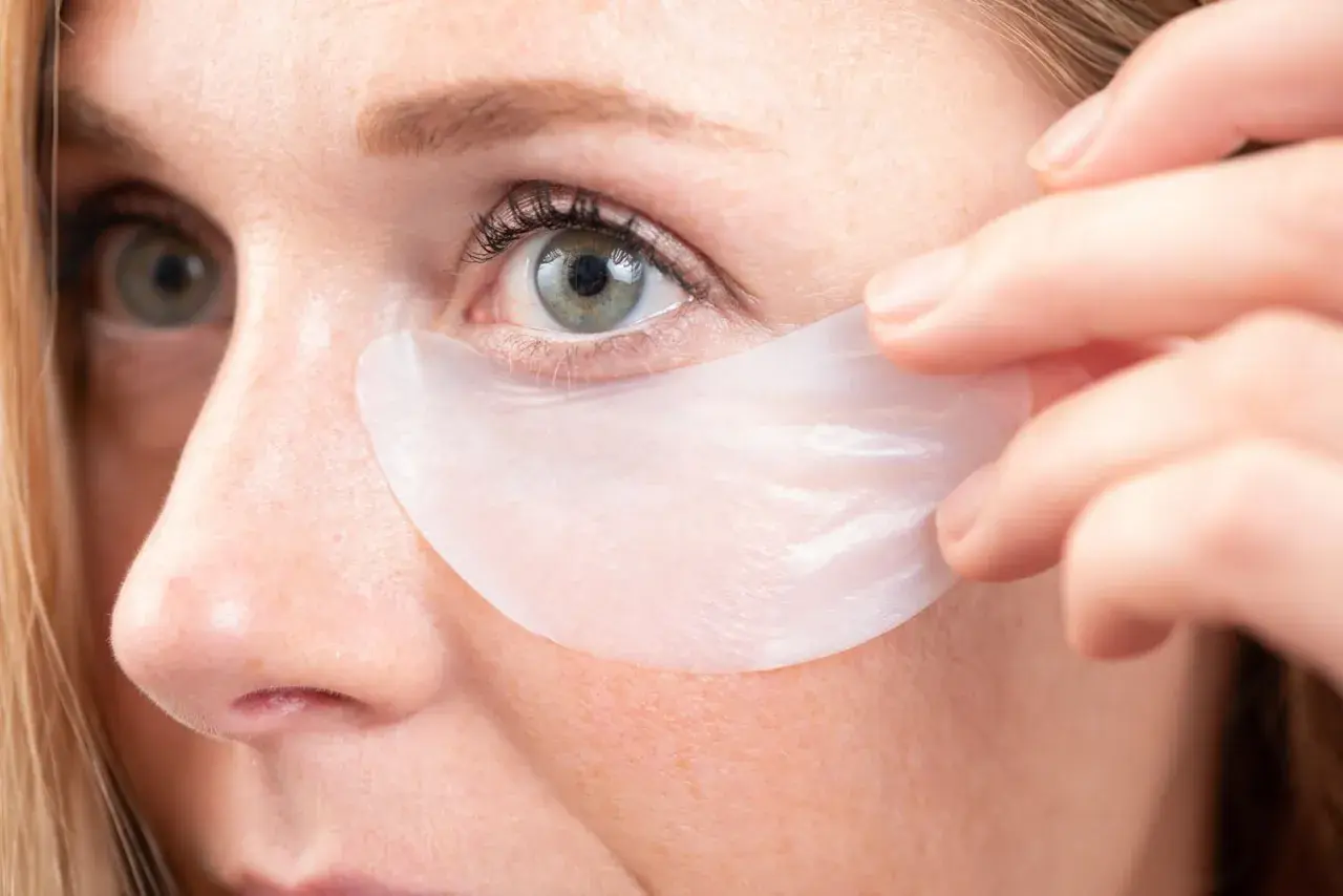 Aplicación de parches para el contorno de ojos. Una mujer se coloca un parche debajo del ojo para hidratar y revitalizar la piel.