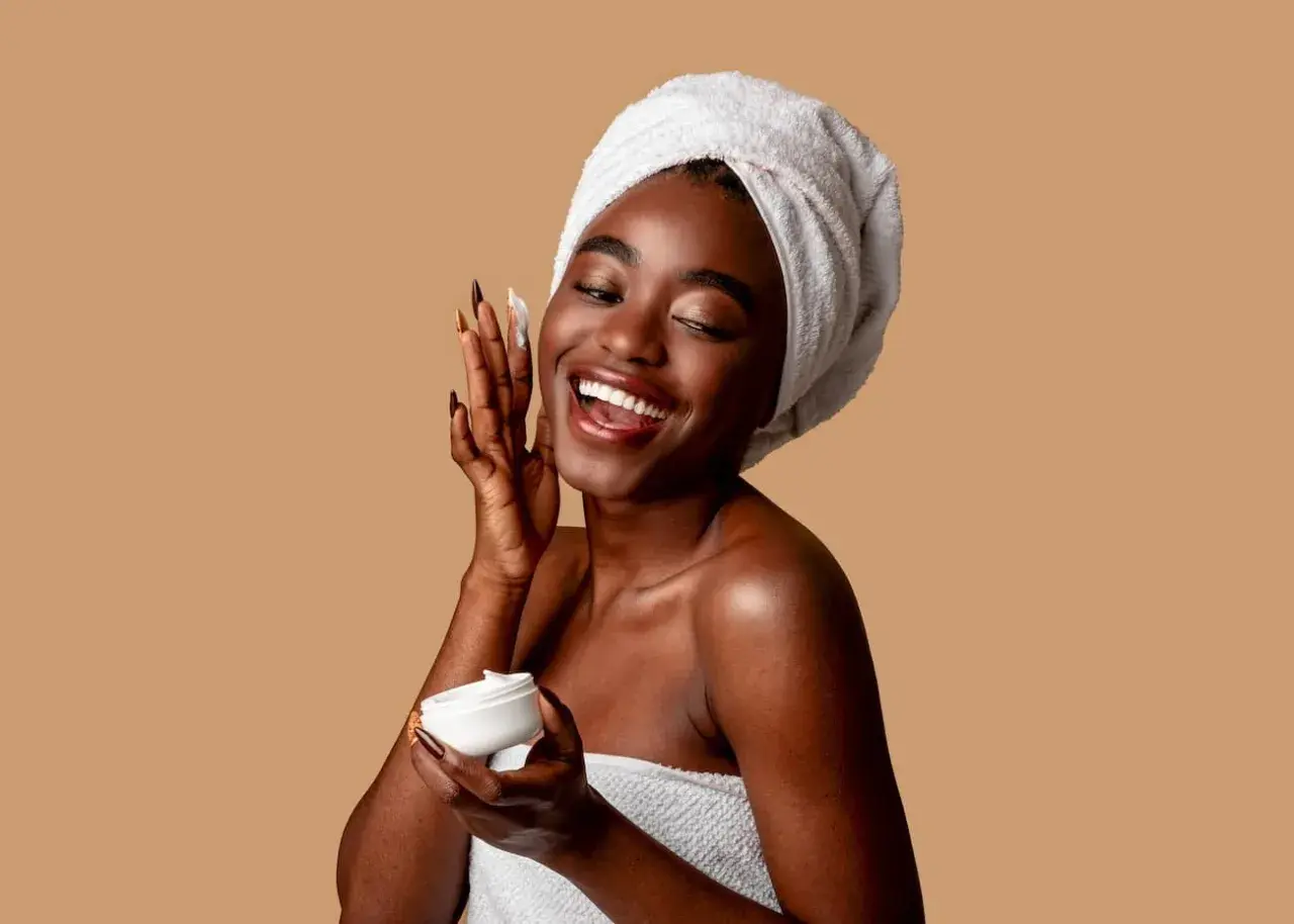 Mujer sonriente con toalla en la cabeza aplica crema con niacinamida y ácido salicílico.