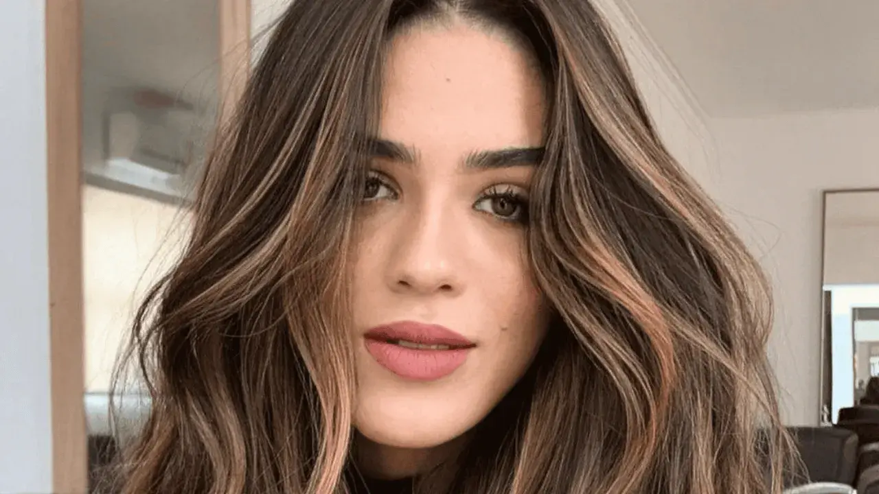 Mujer con cabello castaño oscuro y ondas suaves, resaltado por mechas shatush que aportan luz y dimensión.
