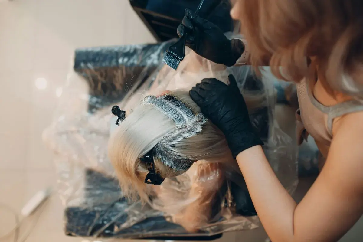 Manos enguantadas aplican tinte al cabello rubio. Es tiempo de tinte pelo para un cambio de look.