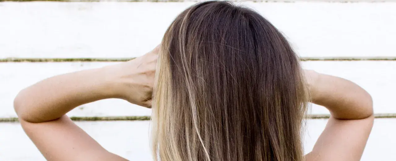 Cabello castaño con reflejos rubios, con las manos detrás de la cabeza.