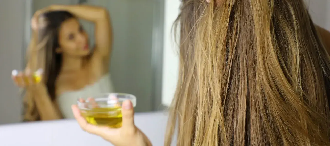 Mujer se aplica aceite de oliva en el pelo, demostrando que el aceite de oliva es bueno para el pelo.