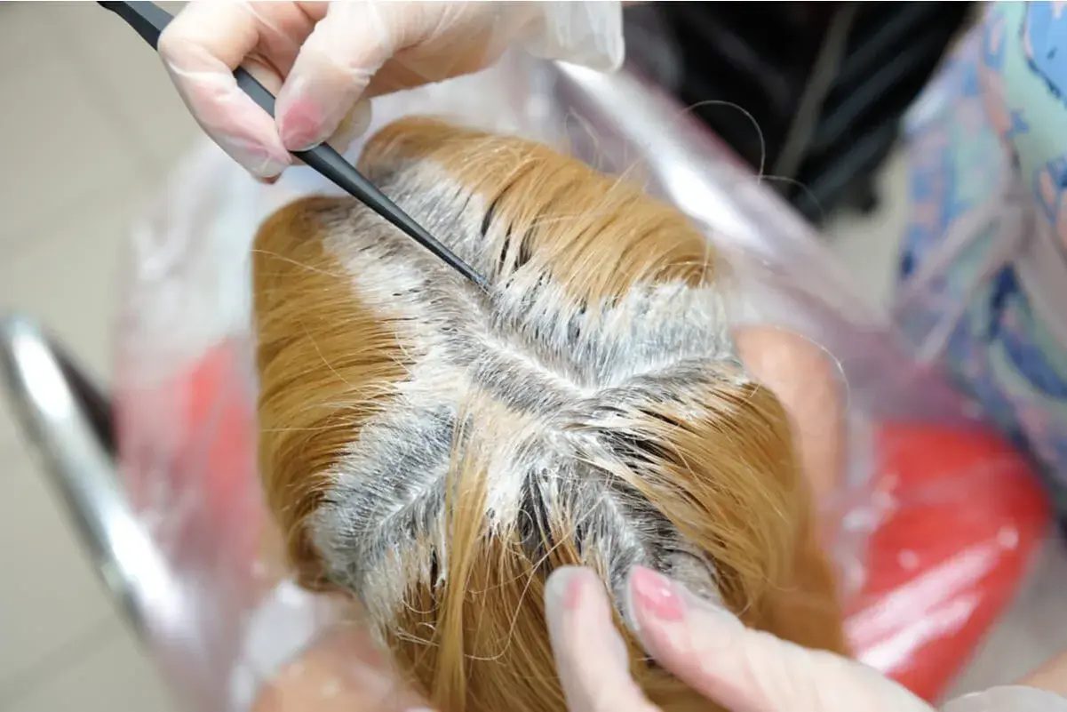 Manos enguantadas aplican decolorante en el cabello rubio. Guía para como decolorar el pelo en casa.