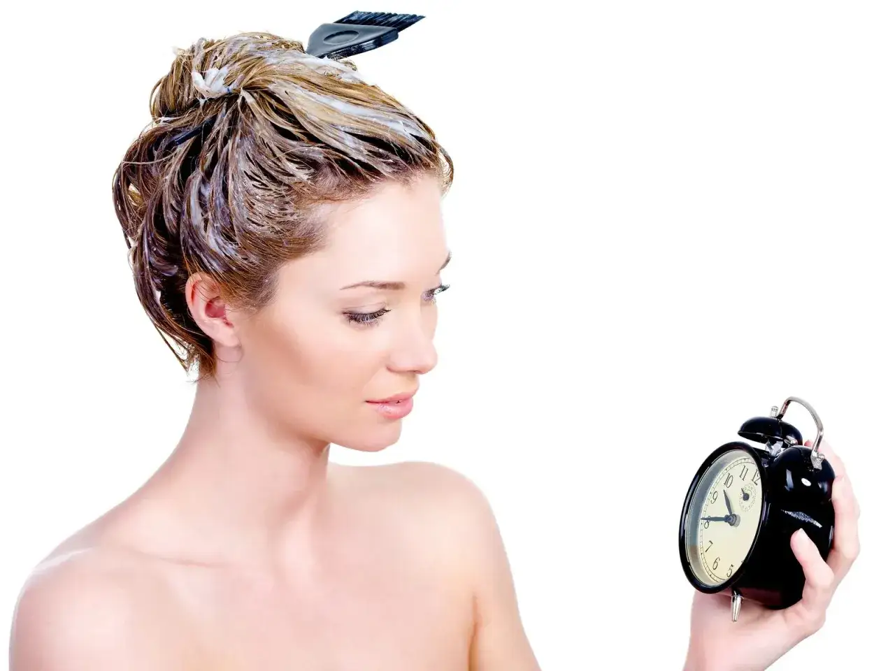 Mujer con tinte en el pelo, revisando el tiempo en un reloj despertador.
