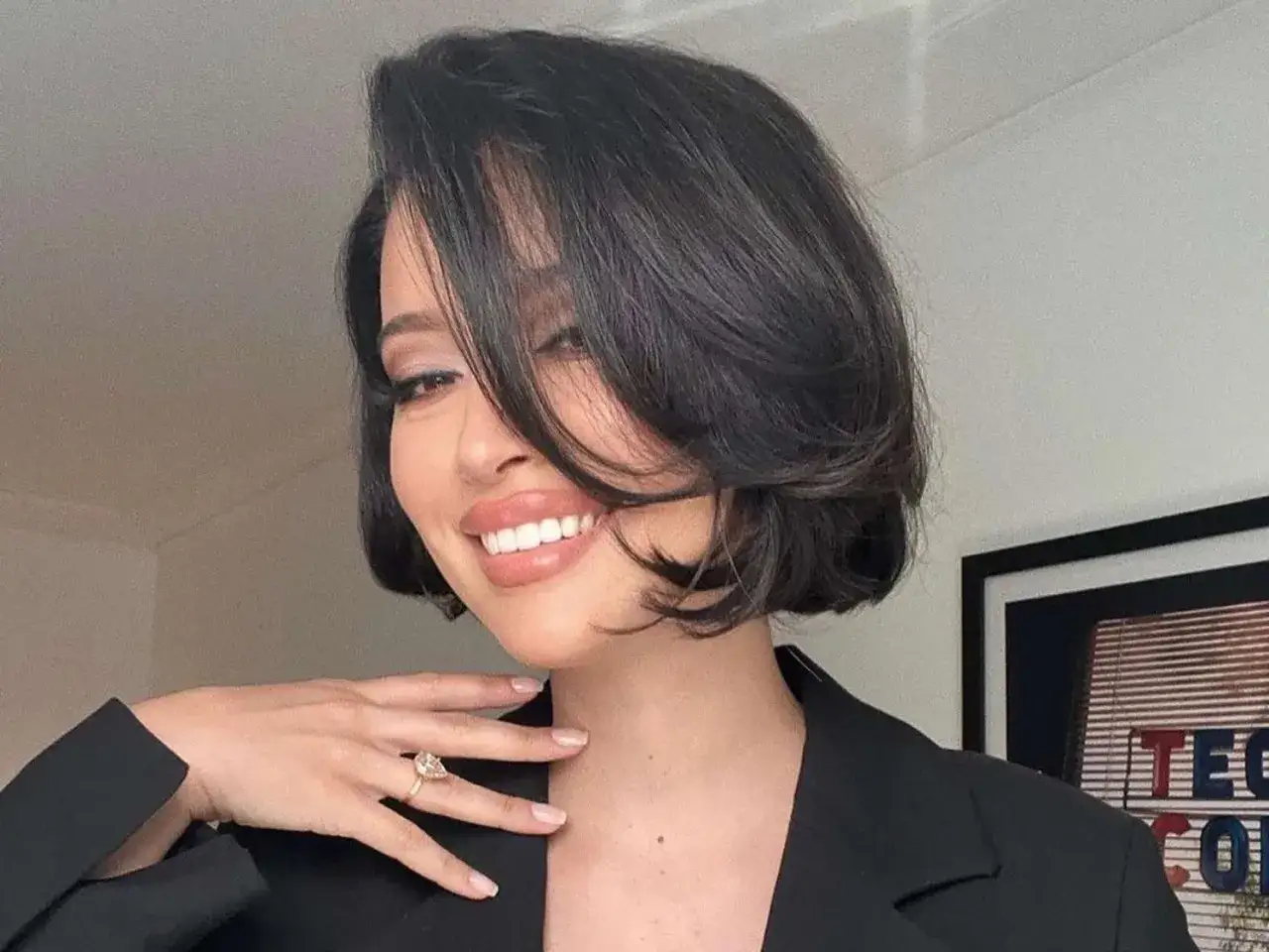 Mujer sonríe con su pelo liso natural, peinado en capas, y un anillo de compromiso.